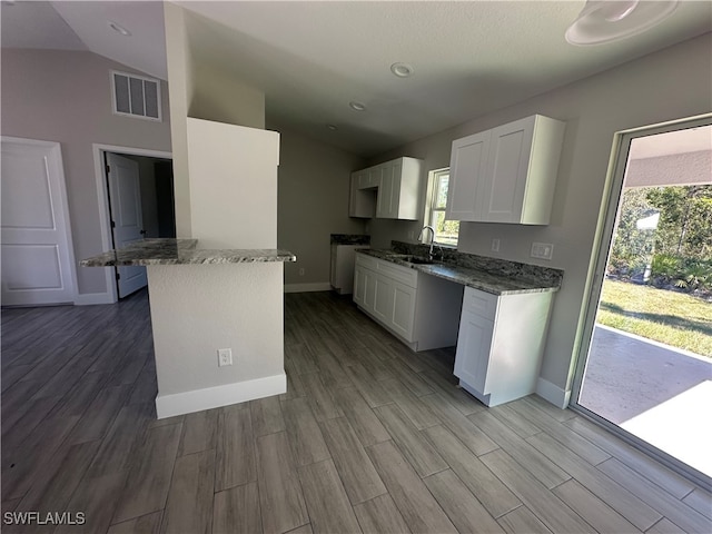 kitchen with lofted ceiling, white cabinets, sink, hardwood / wood-style flooring, and dark stone countertops