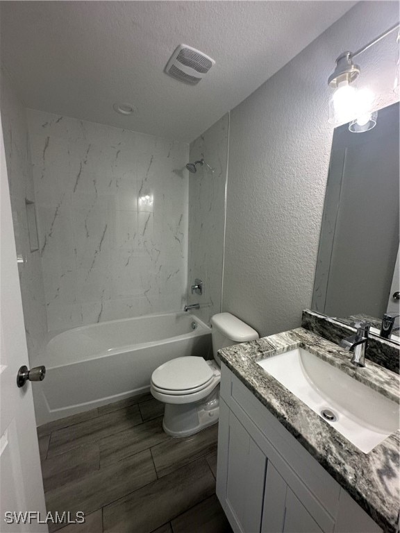 full bathroom featuring toilet, a textured ceiling, vanity, and tiled shower / bath combo