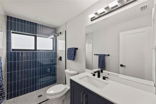 bathroom featuring a tile shower, vanity, and toilet