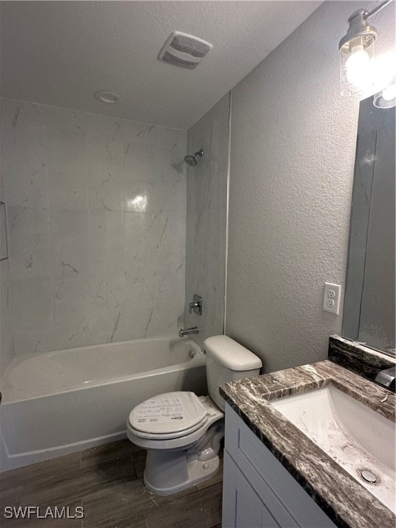 full bathroom with tiled shower / bath combo, wood-type flooring, a textured ceiling, toilet, and vanity