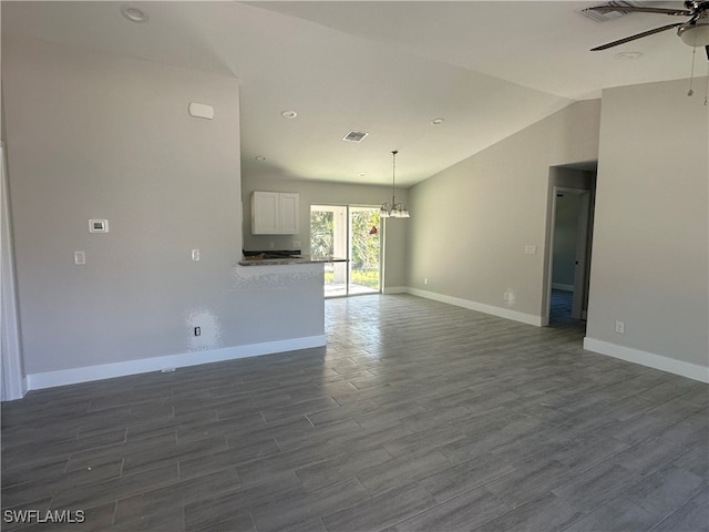 unfurnished living room featuring ceiling fan with notable chandelier, dark wood-type flooring, and vaulted ceiling