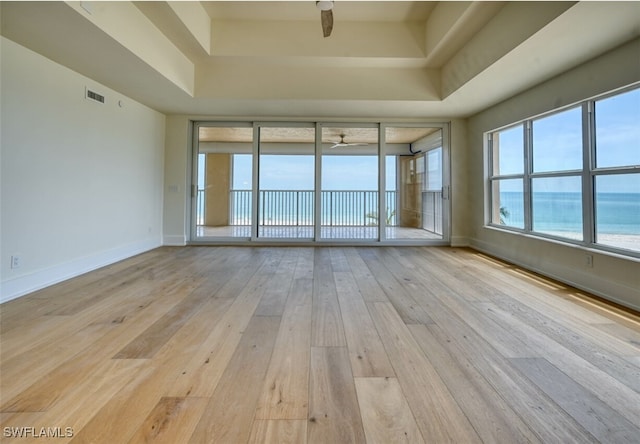 empty room featuring a water view, light hardwood / wood-style flooring, a wealth of natural light, and ceiling fan