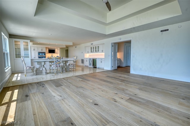 unfurnished living room with light wood-type flooring and a tray ceiling