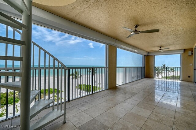 view of patio with ceiling fan, a balcony, a water view, and a beach view