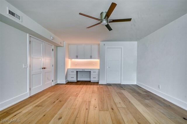 interior space with ceiling fan, built in desk, and light hardwood / wood-style floors