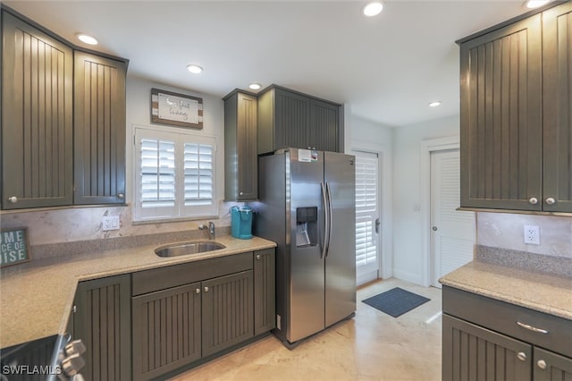 kitchen with light stone countertops, stainless steel fridge with ice dispenser, backsplash, and sink