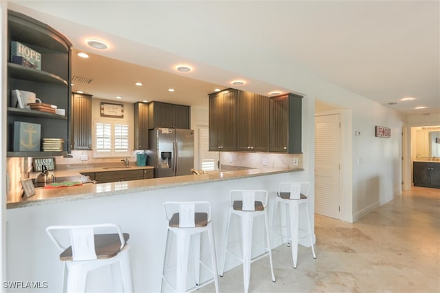 kitchen with sink, stainless steel refrigerator with ice dispenser, dark brown cabinets, a kitchen bar, and kitchen peninsula