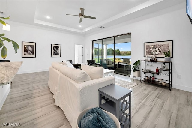 living room with a tray ceiling, ceiling fan, and light hardwood / wood-style floors