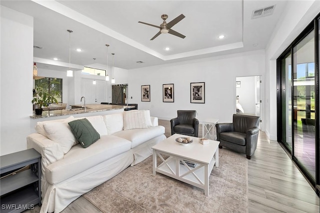 living room featuring ceiling fan, light hardwood / wood-style floors, a wealth of natural light, and a tray ceiling