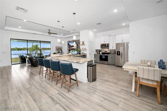 kitchen featuring pendant lighting, ceiling fan, light stone counters, white cabinetry, and stainless steel appliances