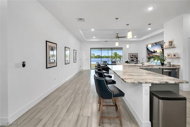 kitchen with pendant lighting, light wood-type flooring, a raised ceiling, and ceiling fan