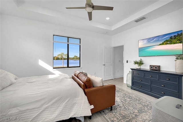 bedroom featuring ceiling fan, light wood-type flooring, and a tray ceiling