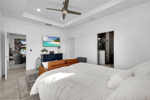 bedroom with ceiling fan, a tray ceiling, and light hardwood / wood-style flooring