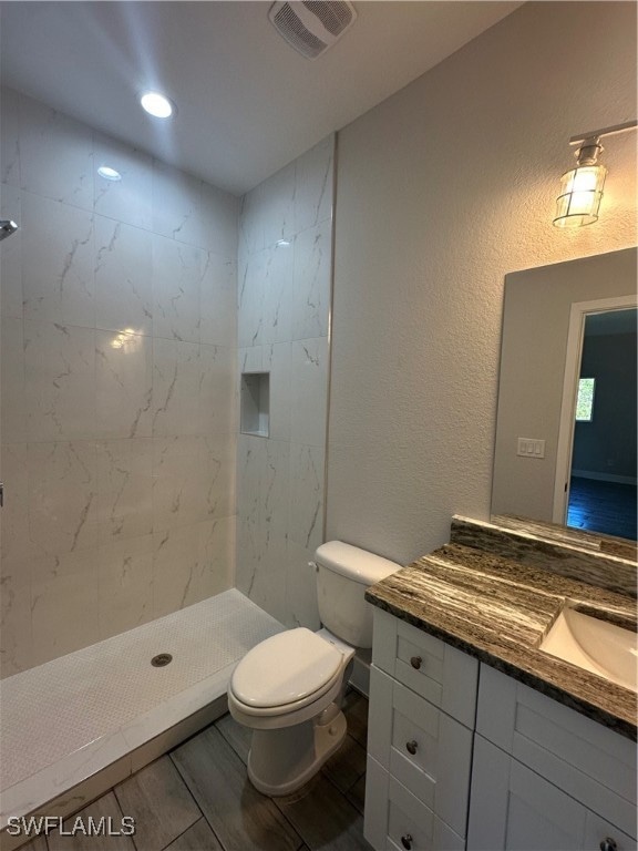 bathroom featuring tiled shower, hardwood / wood-style floors, vanity, and toilet