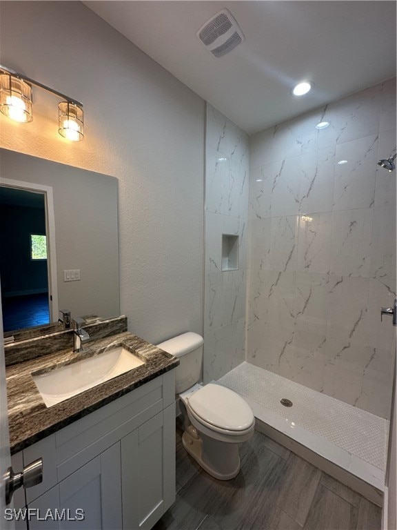 bathroom with vanity, toilet, and a tile shower