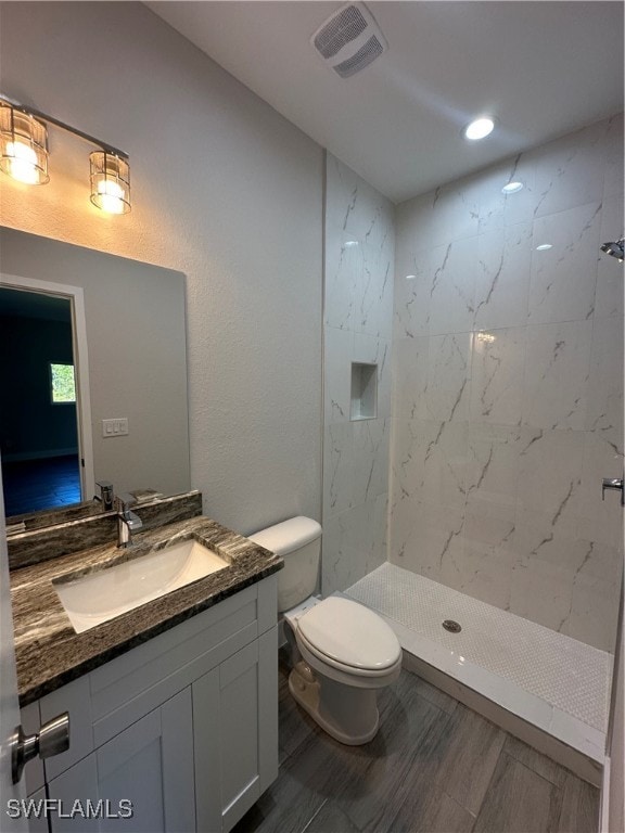 bathroom with a tile shower, vanity, and toilet