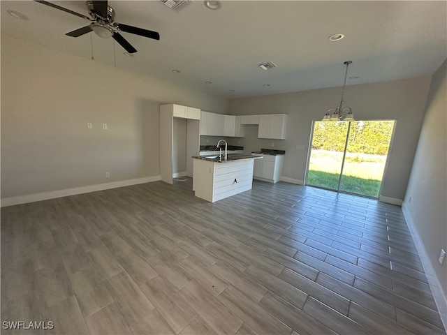 kitchen featuring white cabinets, light wood-type flooring, a center island with sink, and hanging light fixtures