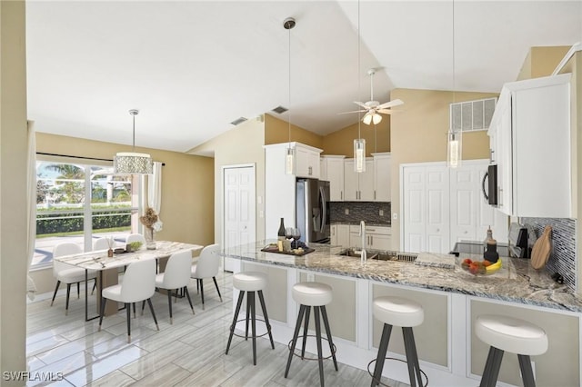 kitchen with kitchen peninsula, backsplash, stainless steel appliances, decorative light fixtures, and white cabinetry