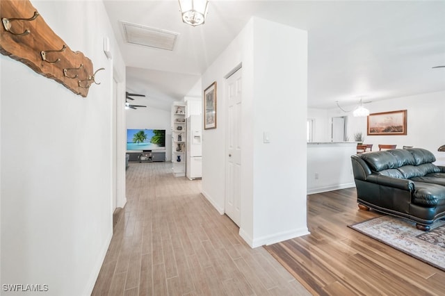 hallway with a chandelier, light hardwood / wood-style floors, and vaulted ceiling