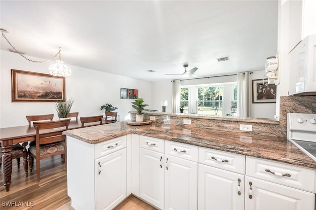 kitchen featuring kitchen peninsula, white appliances, white cabinets, ceiling fan with notable chandelier, and light wood-type flooring