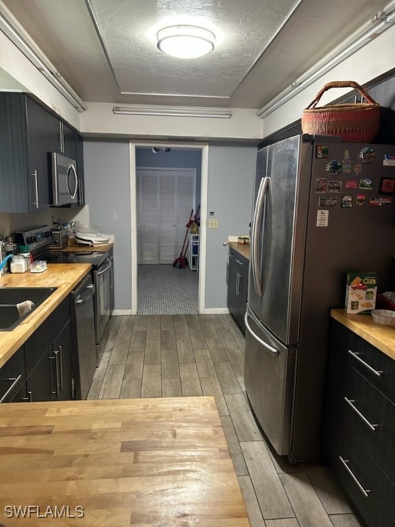 kitchen with sink, light hardwood / wood-style flooring, appliances with stainless steel finishes, and wood counters