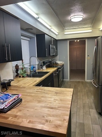 kitchen with wood counters, appliances with stainless steel finishes, light wood-type flooring, a textured ceiling, and sink