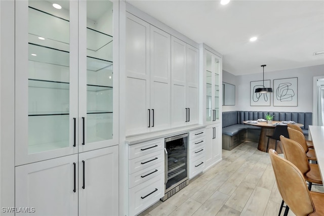 interior space with white cabinets, decorative light fixtures, light hardwood / wood-style floors, and wine cooler