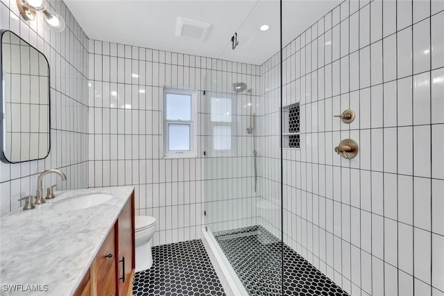 bathroom with a tile shower, vanity, tile walls, tile patterned flooring, and toilet