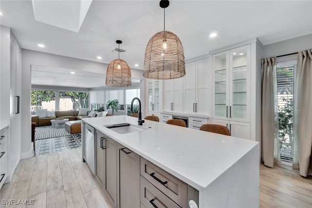 kitchen featuring sink, light wood-type flooring, an island with sink, decorative light fixtures, and white cabinetry