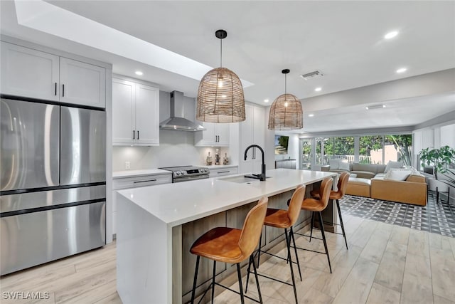 kitchen with appliances with stainless steel finishes, an island with sink, wall chimney exhaust hood, and sink