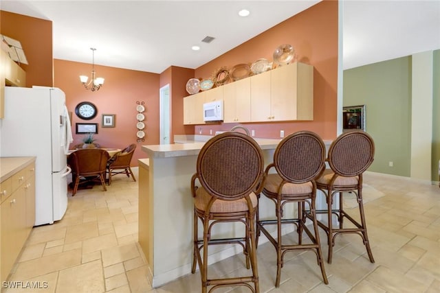 kitchen with kitchen peninsula, white appliances, an inviting chandelier, hanging light fixtures, and a breakfast bar area