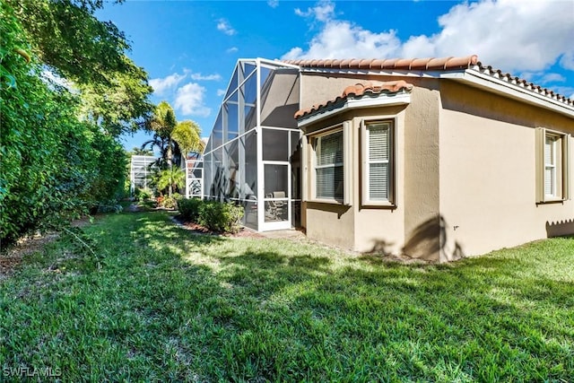 view of side of home with a lawn and glass enclosure