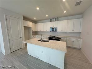 kitchen featuring white cabinetry, sink, black range with electric cooktop, light hardwood / wood-style flooring, and a center island with sink