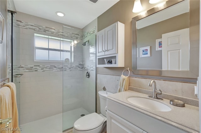 bathroom featuring vanity, toilet, a shower with door, and backsplash