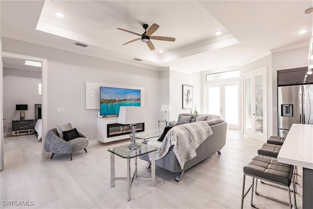 living room featuring french doors, a raised ceiling, ceiling fan, light wood-type flooring, and ornamental molding