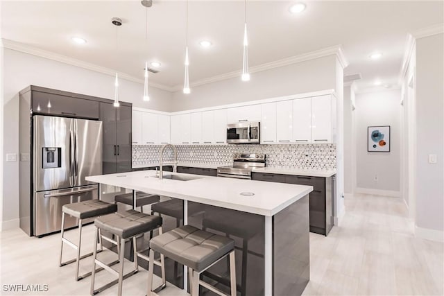 kitchen with sink, stainless steel appliances, crown molding, pendant lighting, and a kitchen island with sink