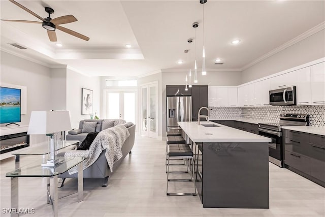 kitchen featuring sink, decorative backsplash, an island with sink, appliances with stainless steel finishes, and decorative light fixtures