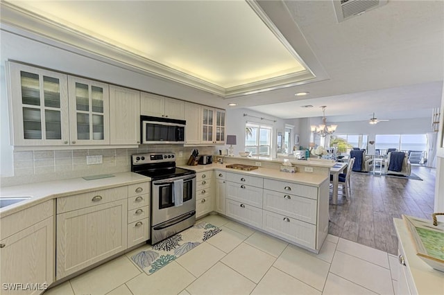 kitchen with backsplash, kitchen peninsula, appliances with stainless steel finishes, ceiling fan with notable chandelier, and light wood-type flooring