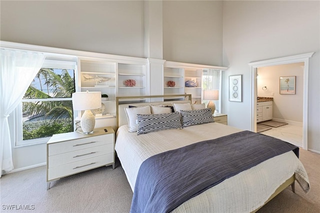 carpeted bedroom featuring ensuite bath, a towering ceiling, and multiple windows