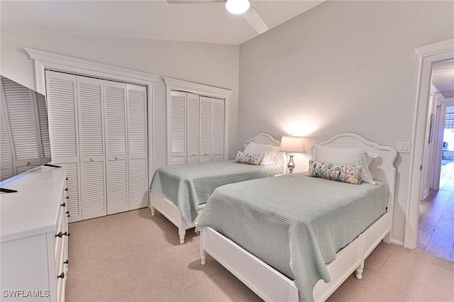 bedroom with ceiling fan, lofted ceiling, light carpet, and two closets