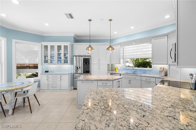 kitchen featuring appliances with stainless steel finishes, light stone counters, a kitchen island, white cabinetry, and hanging light fixtures