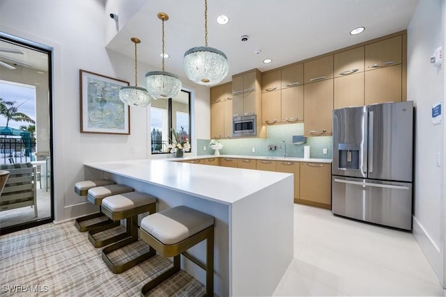 kitchen featuring light brown cabinetry, hanging light fixtures, kitchen peninsula, and appliances with stainless steel finishes