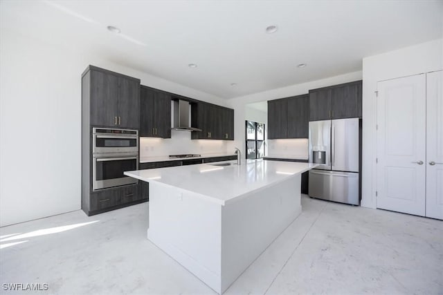 kitchen with sink, stainless steel appliances, wall chimney exhaust hood, and a center island with sink