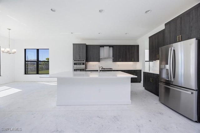 kitchen featuring appliances with stainless steel finishes, pendant lighting, dark brown cabinetry, a center island with sink, and wall chimney exhaust hood