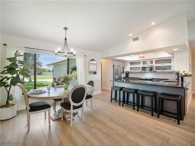 dining room with light wood-type flooring, vaulted ceiling, a notable chandelier, and sink