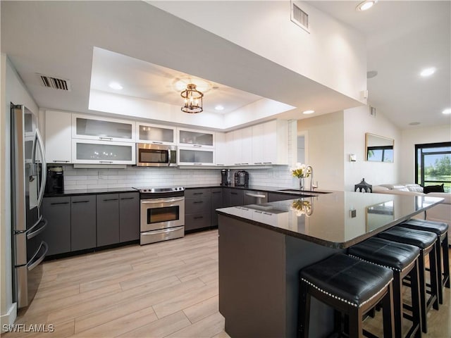 kitchen with sink, stainless steel appliances, a raised ceiling, a kitchen bar, and gray cabinets