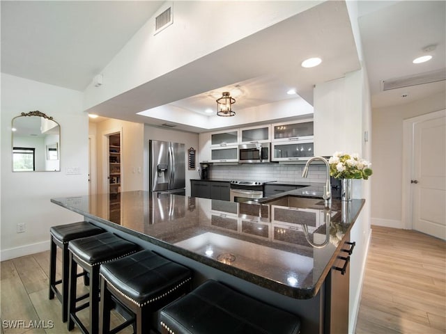 kitchen featuring a breakfast bar, dark stone counters, tasteful backsplash, light hardwood / wood-style floors, and stainless steel appliances