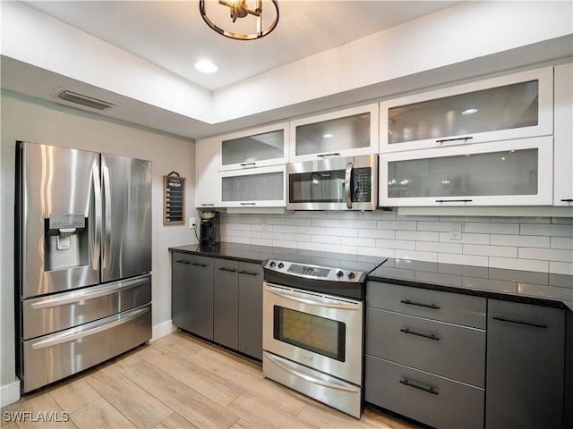 kitchen with gray cabinetry, backsplash, white cabinets, light wood-type flooring, and appliances with stainless steel finishes