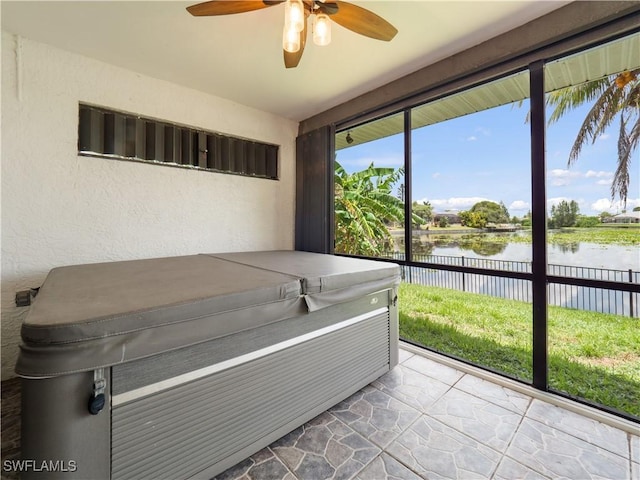 unfurnished sunroom with ceiling fan, a water view, and a hot tub