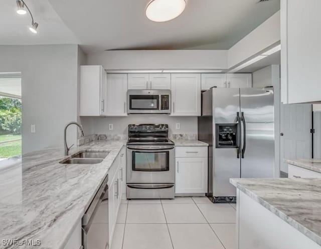 kitchen with light stone countertops, stainless steel appliances, sink, light tile patterned floors, and white cabinetry